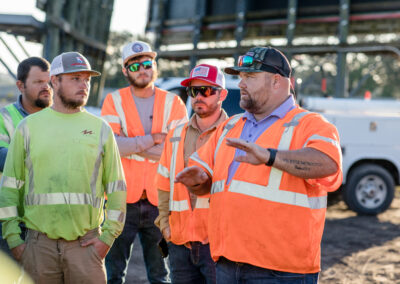 Group of 5 men in orange and yellow safety vests talking