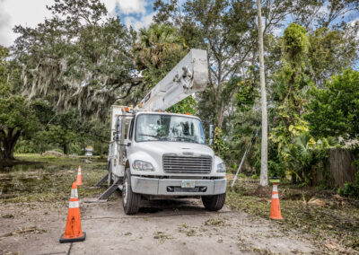 White bucket truck on a dirt road in front of trees with two orange cones out front.