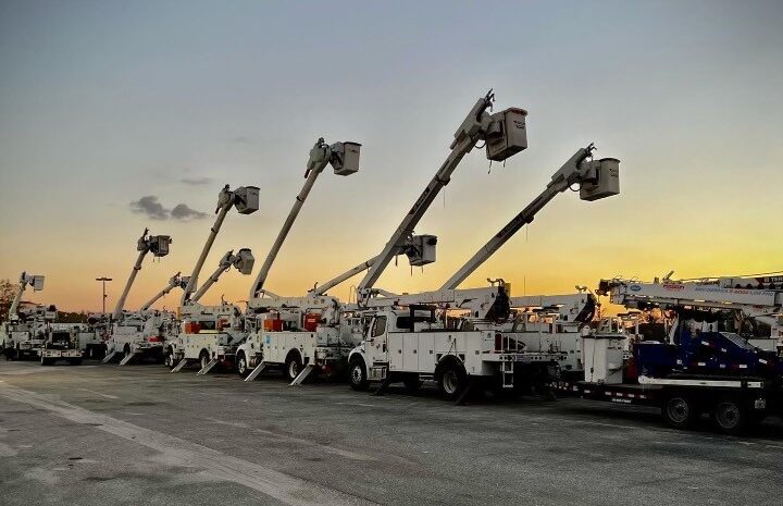 Bucket trucks lined up with booms raised at sunset.